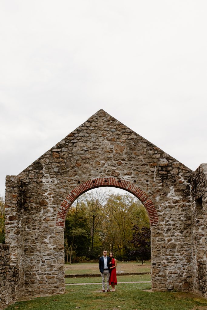 portrait of man and woman in red dress standing under large stone arch