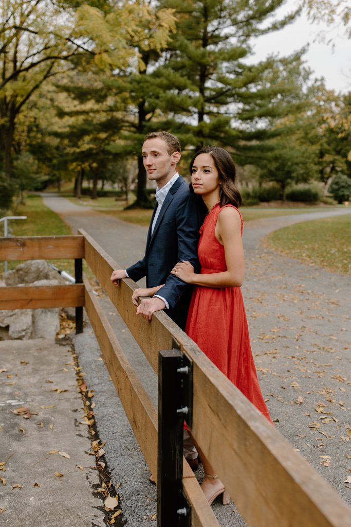 portrait of man and woman in red dress looking off a bridge