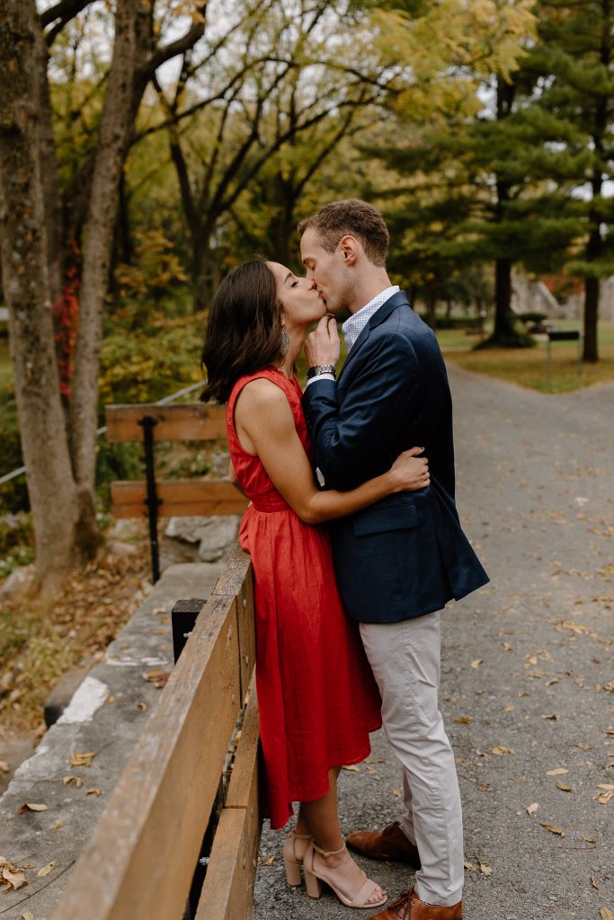 close up portrait of man and woman in red dress standing on a bridge kising