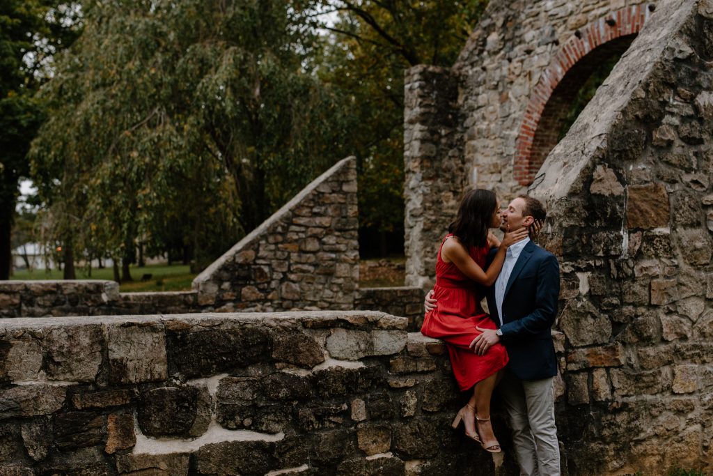 man and woman kissing on stone wall in the rain